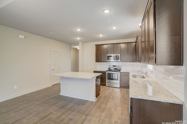 kitchen featuring sink, appliances with stainless steel finishes, tasteful backsplash, light stone countertops, and a kitchen island