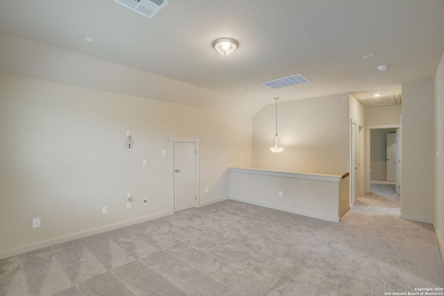 spare room with light colored carpet, vaulted ceiling, and a textured ceiling