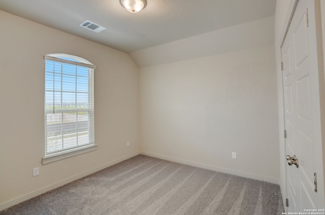 spare room featuring lofted ceiling, carpet floors, and a textured ceiling