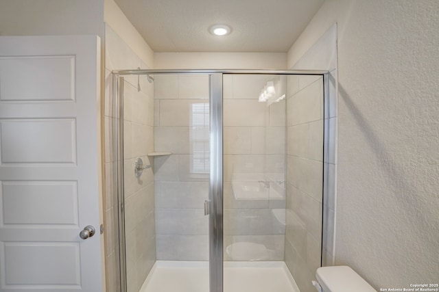 bathroom featuring a shower with door, a textured ceiling, and toilet