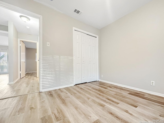 unfurnished bedroom with light wood-style floors, baseboards, visible vents, and a closet