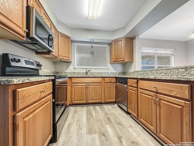 kitchen with light stone counters, appliances with stainless steel finishes, brown cabinetry, a sink, and light wood-type flooring