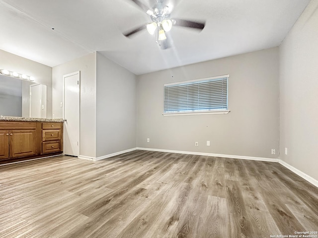 unfurnished bedroom featuring ensuite bathroom, ceiling fan, light wood-style flooring, and baseboards