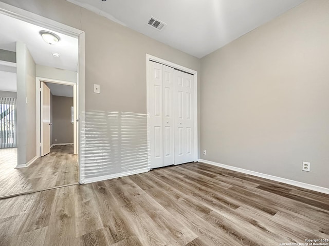 unfurnished bedroom with a closet, wood finished floors, visible vents, and baseboards