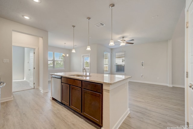 kitchen with an island with sink, sink, stainless steel dishwasher, light stone countertops, and light wood-type flooring