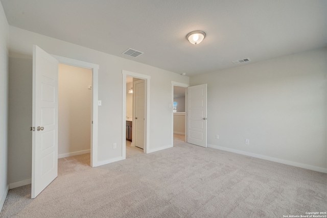 unfurnished bedroom with light colored carpet, ensuite bathroom, and a closet