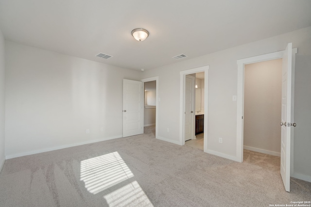 unfurnished bedroom with light carpet, a spacious closet, a closet, and ensuite bathroom