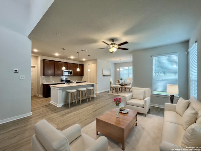 living room featuring ceiling fan, sink, and light wood-type flooring