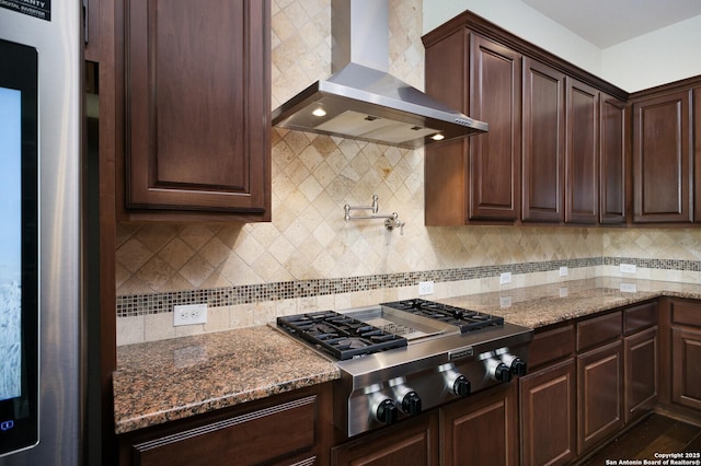 kitchen with wall chimney exhaust hood, stainless steel gas cooktop, refrigerator, dark stone counters, and decorative backsplash