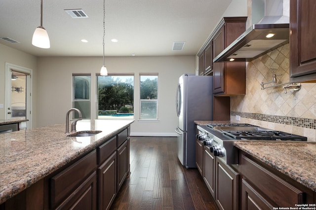 kitchen featuring hanging light fixtures, backsplash, stainless steel appliances, light stone counters, and wall chimney exhaust hood