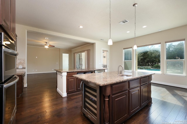 kitchen featuring sink, hanging light fixtures, appliances with stainless steel finishes, an island with sink, and beverage cooler