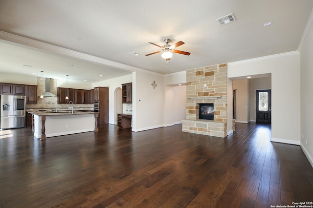 unfurnished living room featuring a stone fireplace, sink, ceiling fan, crown molding, and dark wood-type flooring