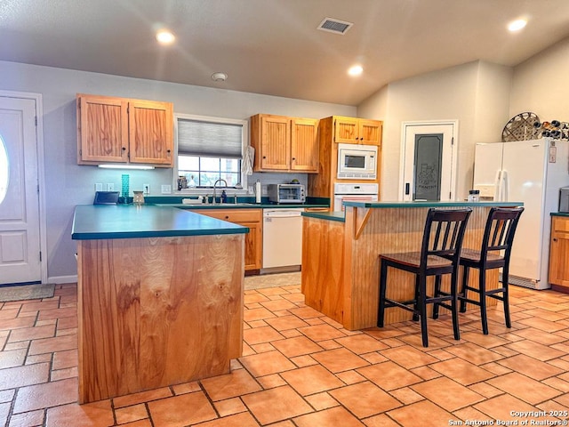 kitchen with a kitchen breakfast bar, a kitchen island, sink, and white appliances