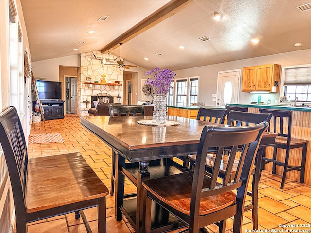 dining room with lofted ceiling with beams, ceiling fan, sink, and a fireplace