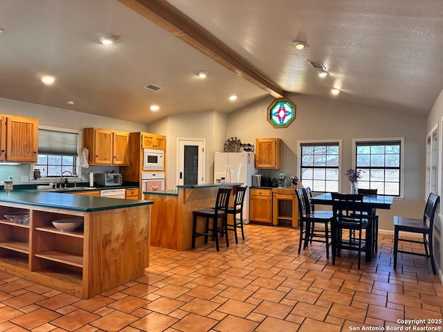 kitchen featuring sink, vaulted ceiling with beams, a kitchen breakfast bar, a kitchen island, and white appliances