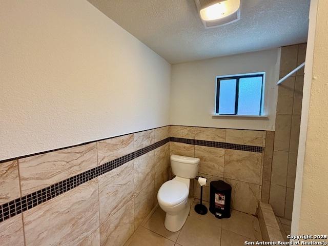 bathroom with tile walls, walk in shower, toilet, tile patterned floors, and a textured ceiling