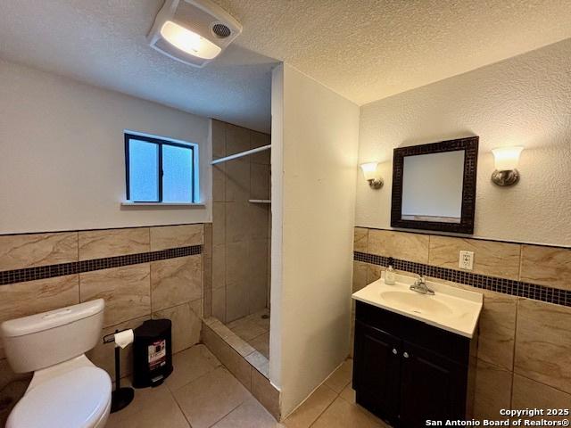 bathroom with tile patterned floors, toilet, a textured ceiling, and a tile shower