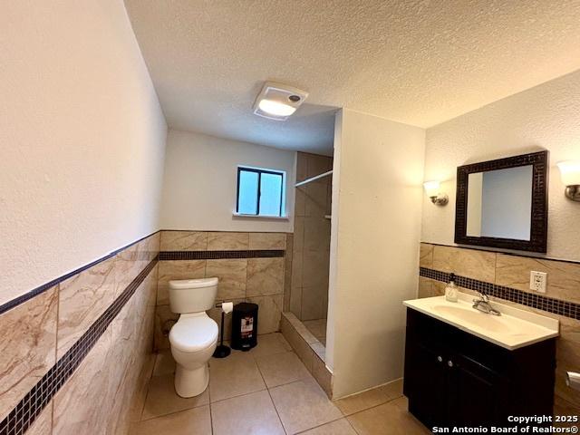 bathroom featuring tiled shower, toilet, tile walls, a textured ceiling, and vanity