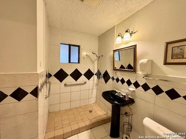 bathroom with tile patterned flooring, tile walls, a textured ceiling, and a tile shower