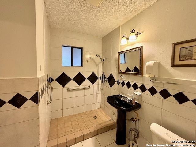 bathroom featuring a tile shower, tile patterned flooring, a textured ceiling, and tile walls