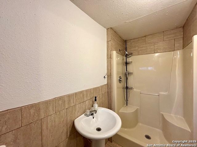 bathroom featuring tile walls, sink, a textured ceiling, and tiled shower