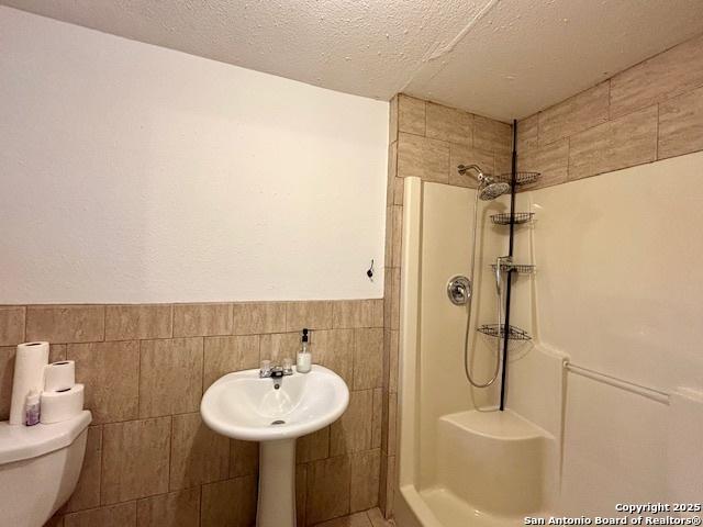 bathroom featuring tile walls, a textured ceiling, toilet, and tiled shower