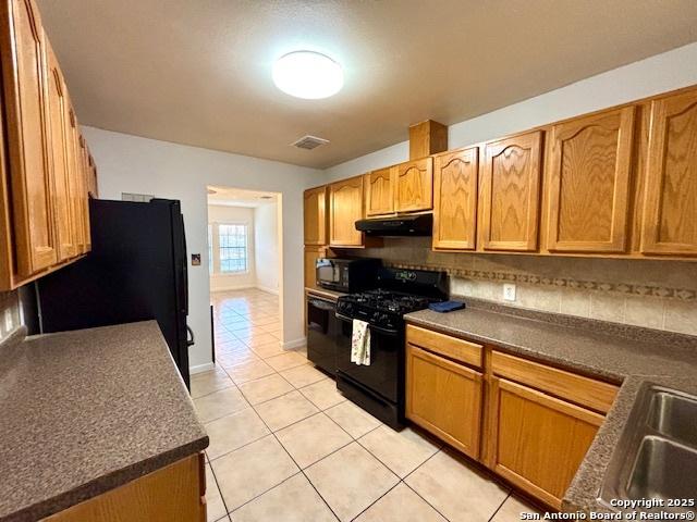 kitchen with tasteful backsplash, sink, light tile patterned floors, and black appliances