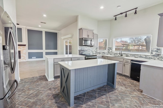 kitchen with sink, track lighting, appliances with stainless steel finishes, gray cabinets, and a kitchen island