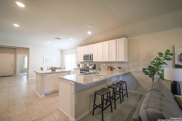 kitchen with a breakfast bar area, white cabinets, light stone counters, kitchen peninsula, and stainless steel appliances