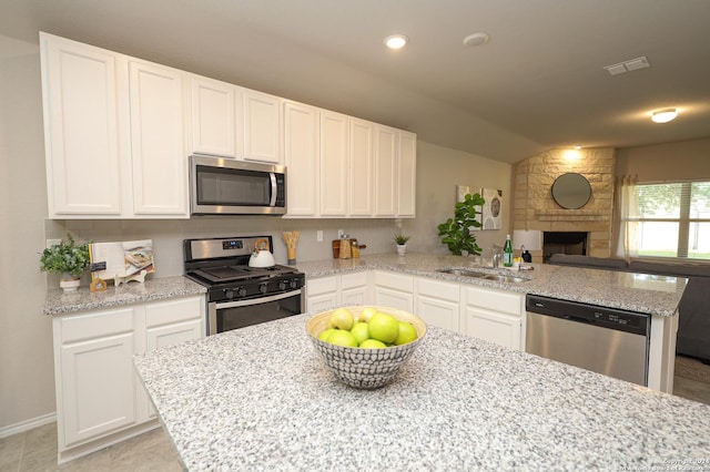 kitchen with lofted ceiling, sink, light stone counters, appliances with stainless steel finishes, and white cabinets