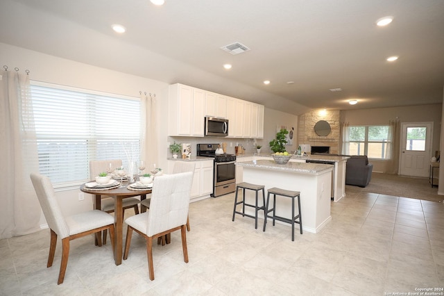 kitchen featuring a kitchen bar, white cabinetry, a kitchen island, stainless steel appliances, and light stone countertops