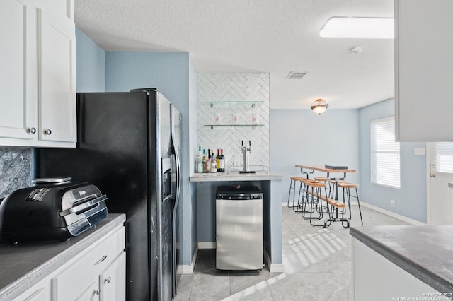 kitchen with white cabinetry, a textured ceiling, backsplash, and stainless steel refrigerator