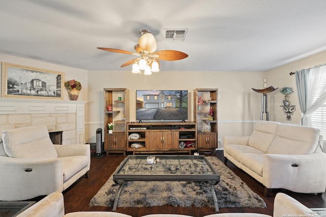 living room featuring a stone fireplace, dark wood-type flooring, and ceiling fan