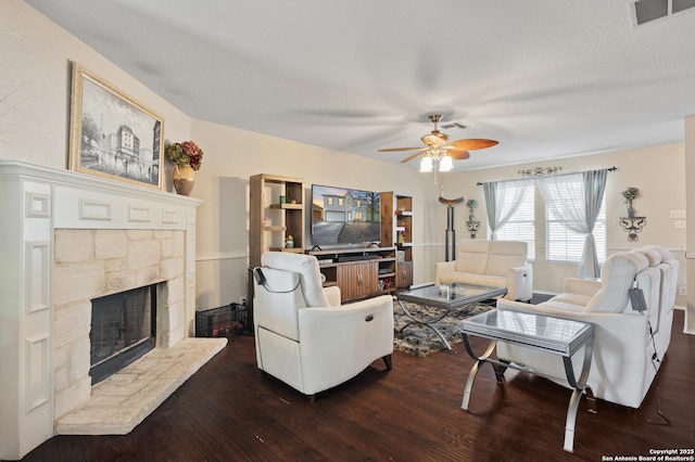 living room featuring ceiling fan, a fireplace, dark hardwood / wood-style flooring, and a textured ceiling