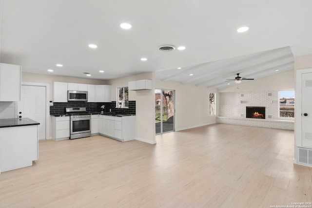 kitchen with stainless steel appliances, vaulted ceiling with beams, white cabinetry, light hardwood / wood-style flooring, and a healthy amount of sunlight