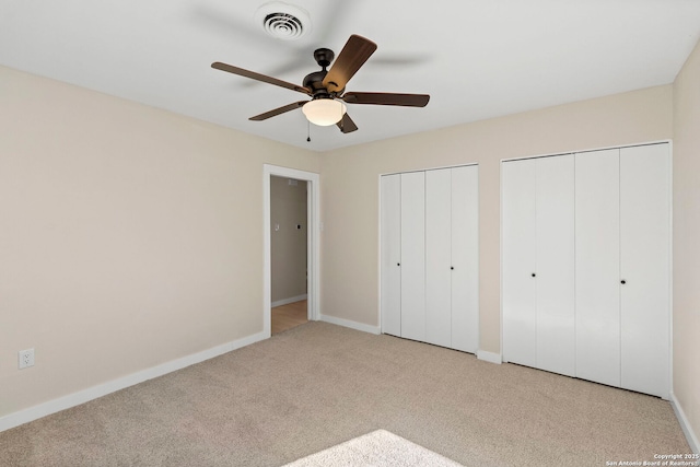 unfurnished bedroom featuring ceiling fan, light colored carpet, and two closets