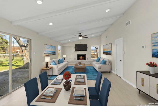 living room featuring ceiling fan, vaulted ceiling with beams, a fireplace, and light hardwood / wood-style flooring