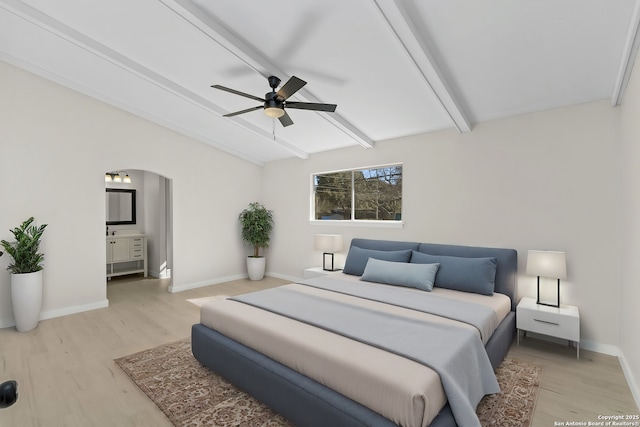 bedroom featuring ceiling fan, ensuite bath, light hardwood / wood-style floors, and vaulted ceiling with beams