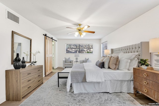 bedroom featuring wood-type flooring, a barn door, and ceiling fan