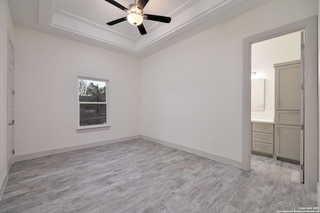 unfurnished bedroom featuring light hardwood / wood-style floors, connected bathroom, ceiling fan, and a tray ceiling