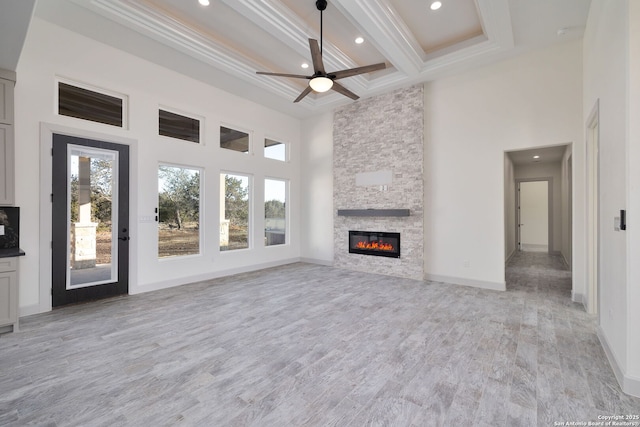 unfurnished living room featuring crown molding, ceiling fan, beam ceiling, a stone fireplace, and light wood-type flooring