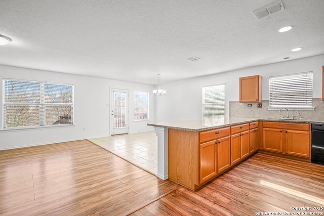 kitchen with pendant lighting, black dishwasher, backsplash, light hardwood / wood-style floors, and kitchen peninsula