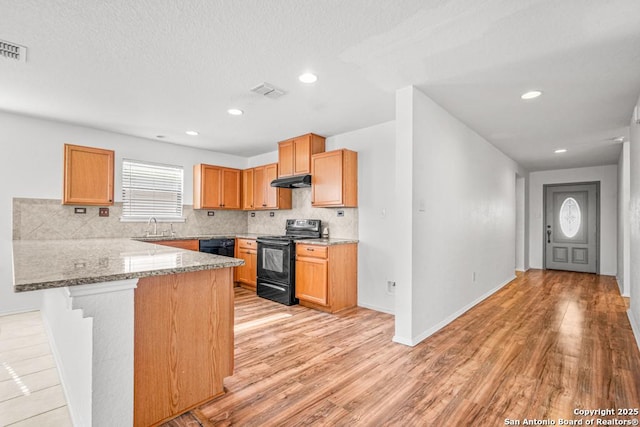 kitchen with a breakfast bar, sink, decorative backsplash, light stone counters, and black appliances