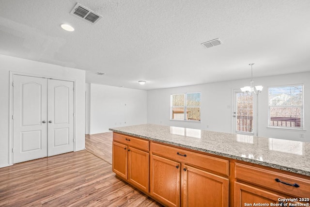 kitchen featuring hanging light fixtures, light stone counters, a notable chandelier, a textured ceiling, and light wood-type flooring