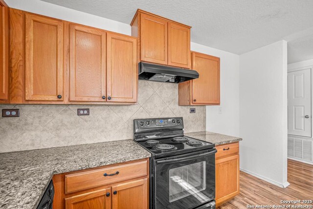 kitchen featuring exhaust hood, light stone counters, tasteful backsplash, light hardwood / wood-style floors, and black appliances