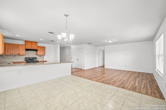 kitchen with sink, light stone counters, black electric range, hanging light fixtures, and backsplash