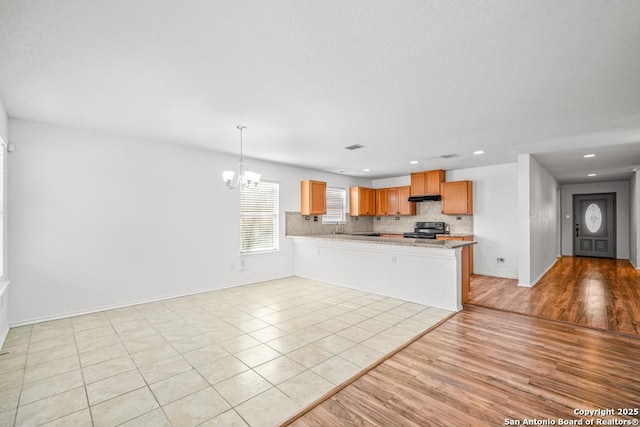 kitchen with an inviting chandelier, hanging light fixtures, electric range, kitchen peninsula, and light hardwood / wood-style floors