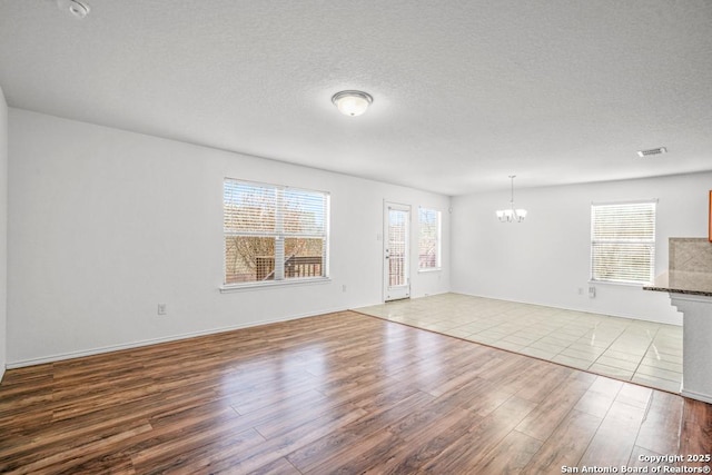 unfurnished living room featuring a textured ceiling, light hardwood / wood-style flooring, and a notable chandelier