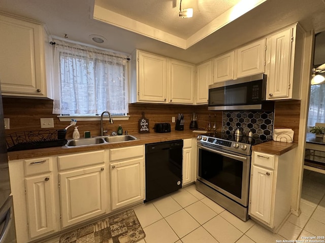 kitchen featuring sink, light tile patterned floors, a raised ceiling, stainless steel appliances, and white cabinets