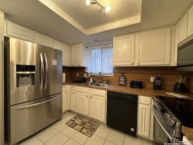 kitchen with appliances with stainless steel finishes, a tray ceiling, sink, and white cabinets